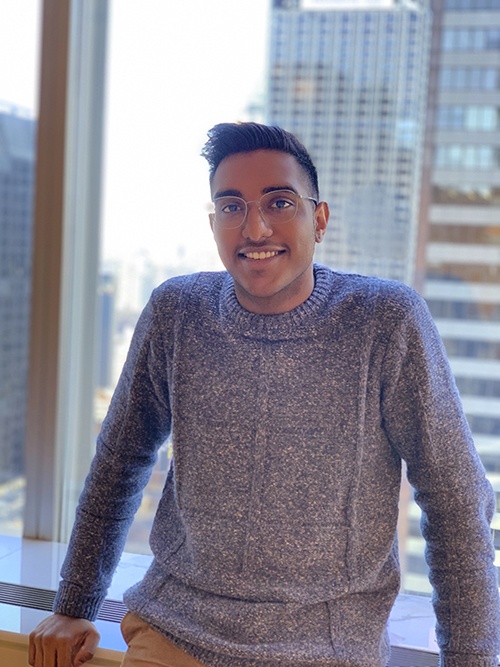 Nick Sookhoo stands in front of a window with skyscrapers in the background